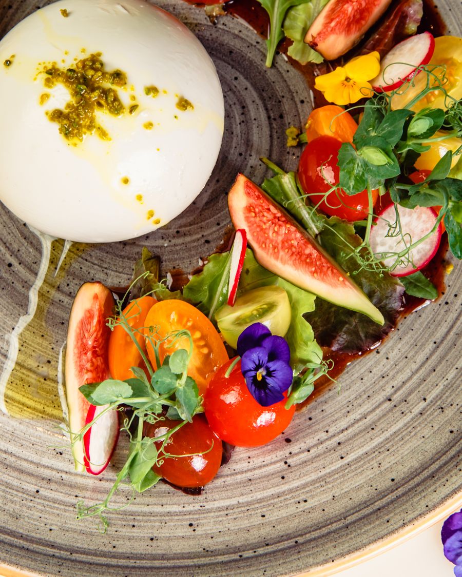 Burrata with heirloom tomatoes, basil oil, and edible flowers on a rustic ceramic plate.