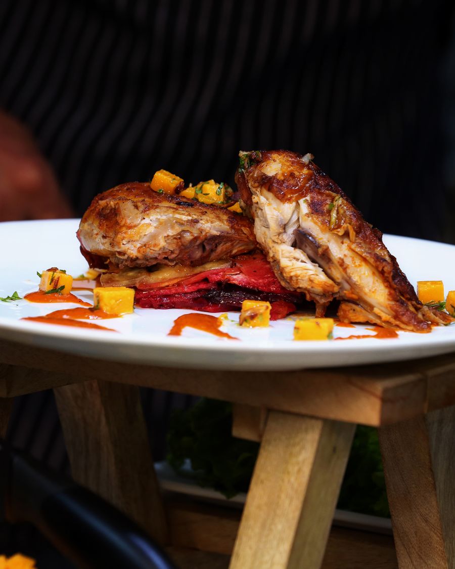 Herb-roasted chicken plated with pan sauce and charred vegetables on a white plate.