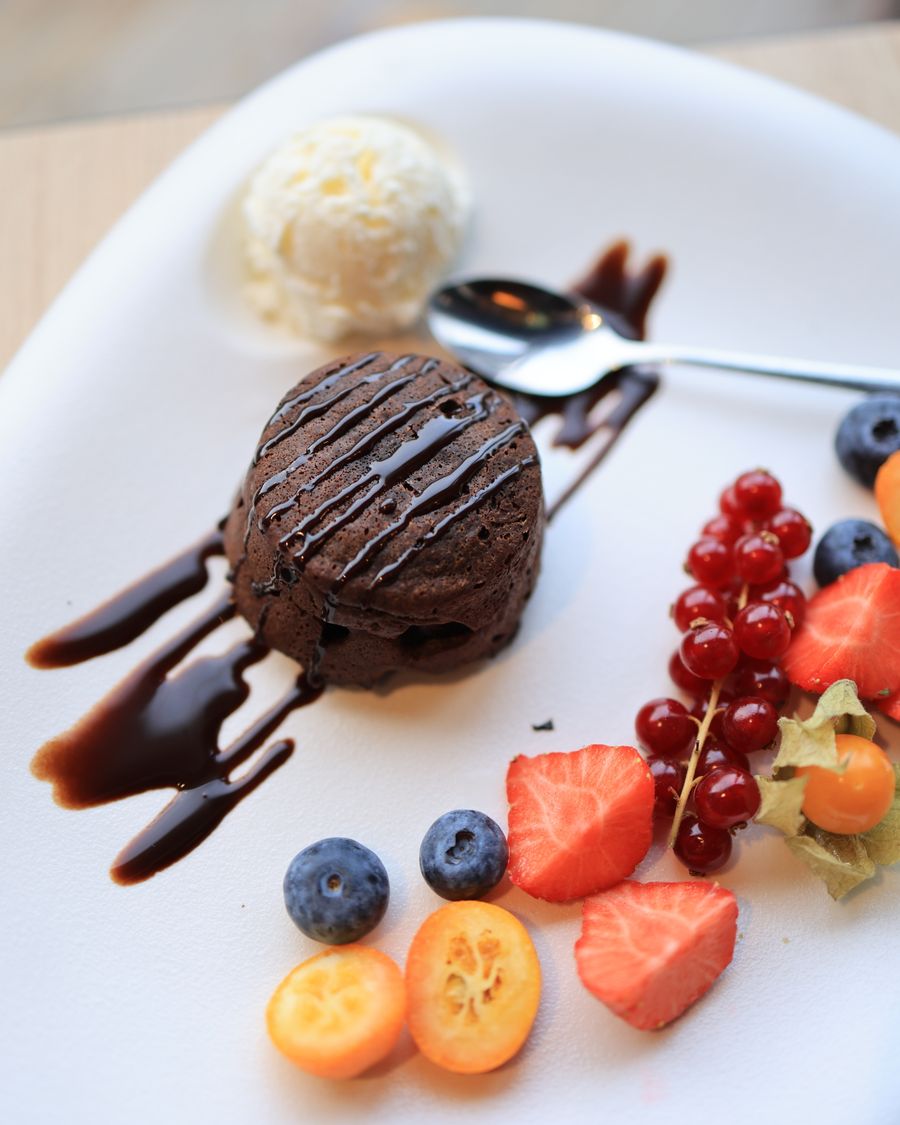 Dark chocolate dessert with berries, sauce, and a quenelle of cream on a white plate.