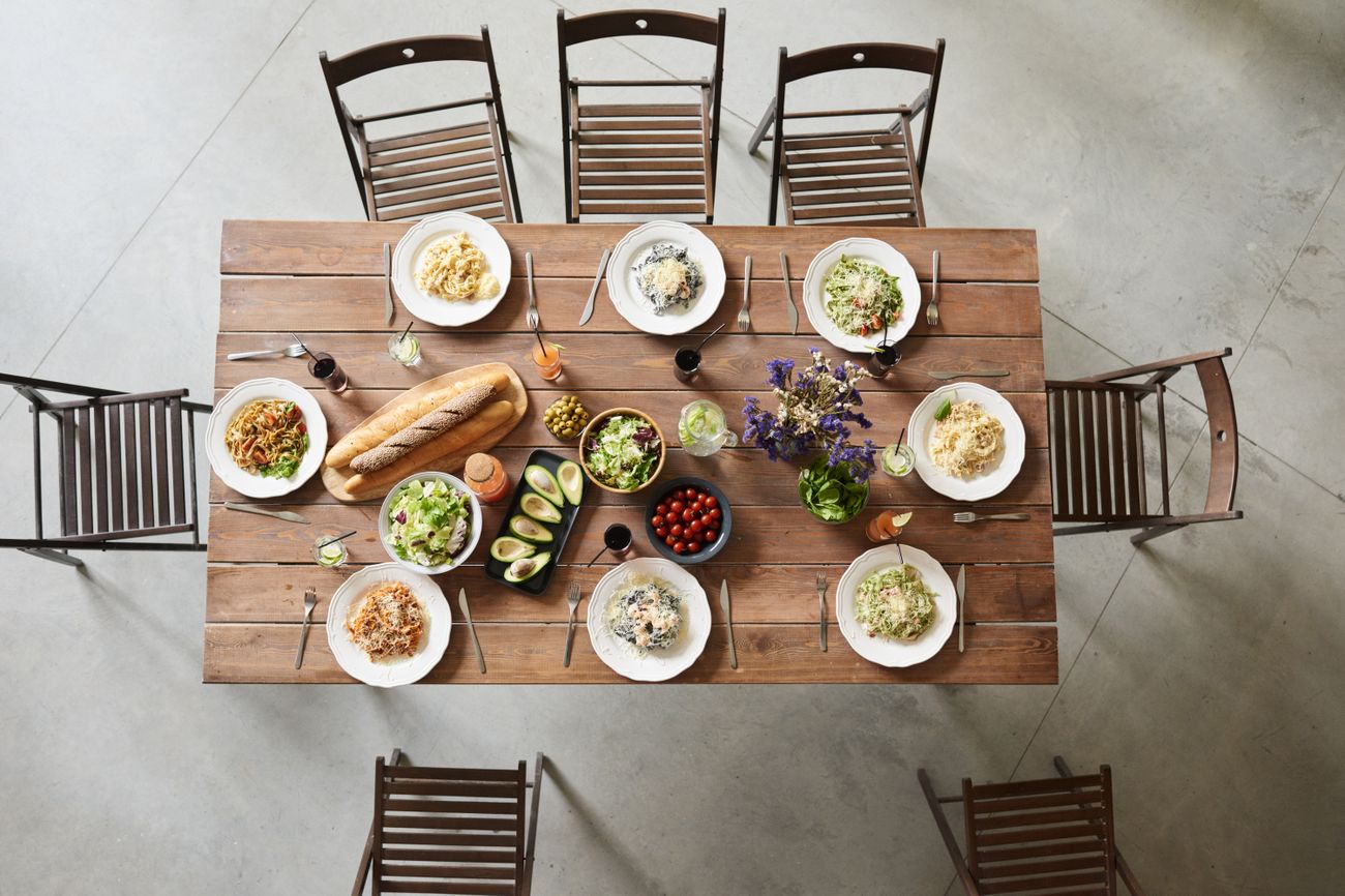 An overhead view of a wooden table filled with shared plates, bread, salads, and drinks.